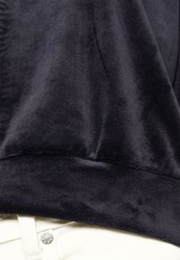 Svart velourtyg med en jämn struktur, med rundad nederkant och sömdetaljer, kombinerat med ljusf ärgad tyg nederst.