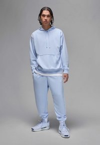 Sweatshirt azul claro com capuz e bolso frontal, combinado com calças de treino a condizer. Apresenta um logótipo branco do lado esquerdo e um tecido texturizado.