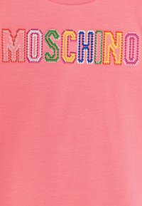 Różowa bawełniana koszulka z haftowanymi literami wy spellującymi "MOSCHINO" w różnych żywych kolorach. Prosty okrągły dekolt i miękka tekstura.
