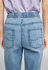 Pantalones de mezclilla en un azul claro con una cintura elástica, dos bolsillos traseros con costura curva y un corte relajado.