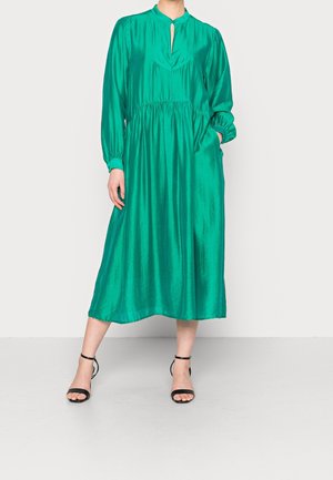 Grøn satin midi kjole med en nøglehul-udskæring, lange ærmer, samlet talje og sidelommer. Sorte strop sandaler.