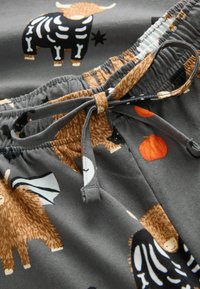 Shorts en tissu gris ornés de divers motifs animaliers, incluant des squelettes, des citrouilles et des accents bruns texturés. Comprend une taille élastique avec cordon de serrage.