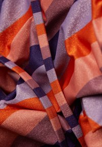 Tissu tissé coloré avec une texture brillante, présentant un motif abstrait de rectangles orange, violet et rose de tailles variées.