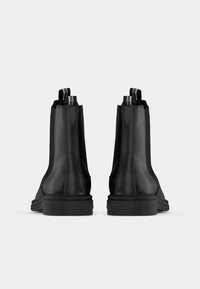 Paire de bottines Chelsea en cuir noir avec languettes, vue de dos sur un fond uni clair.