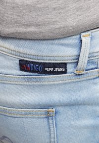 Jeans de mezclilla azul claro con una textura suave. Cuentan con una etiqueta de tela azul oscura con "PEPE JEANS" en blanco, cosida a la cinturilla trasera.