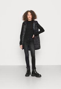 Gilet imbottito nero con cappuccio, abbinato a un top aderente nero a coste e jeans skinny neri. Stivali neri chunky con più cinturini.