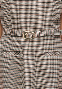 Καρό φόρεμα με μαύρο, λευκό και ροζ μοτίβο· διαθέτει στενή ζώνη με χρυσή αγκράφα και δύο μπροστινές τσέπες. Υφασμένο ύφασμα.