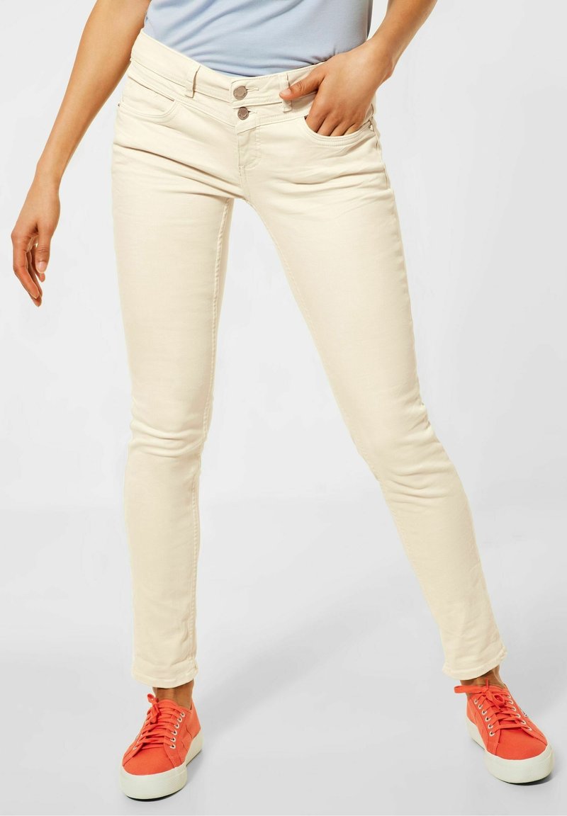 Ljusbeige skinny jeans med en slät textur, med två framfickor och två knäppningar. Matchade med orange sneakers.