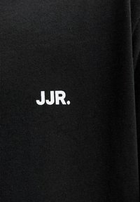 Μαύρο ύφασμα με μικρό λευκό κείμενο "JJR." τυπωμένο σε αυτό, κεντραρισμένο στην ορατή περιοχή.