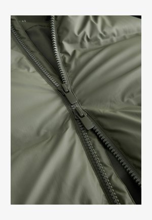 Olivově zelená zateplená bunda s dvojitým zipem, který má texturované černé zuby a hladkou látku. Interiér má měkkou podšívku.