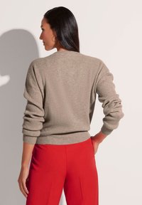 Lichtgrijze geribde trui met lange mouwen en een getailleerde taille. Gecombineerd met felrode broek, wat het kleurcontrast benadrukt.