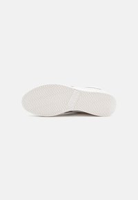 Shoe sole with a textured white rubber material, featuring a herringbone pattern and a rectangular logo design near the heel.