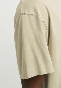 Beige bomulds t-shirt med rund hals, korte ærmer, blød tekstur og synlige sømdetaljer på skulderen og kanten.