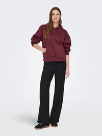 Sweat à capuche bordeaux avec une poche avant et des cordons de serrage, assorti à un pantalon noir à jambes larges. Chaussures noires avec une surface texturée et des lacets.