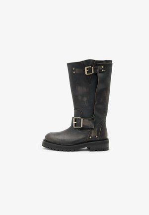 Bota alta de couro preto apresenta fivelas, superfície texturizada, bico arredondado e sola robusta, projetada para durabilidade e suporte.