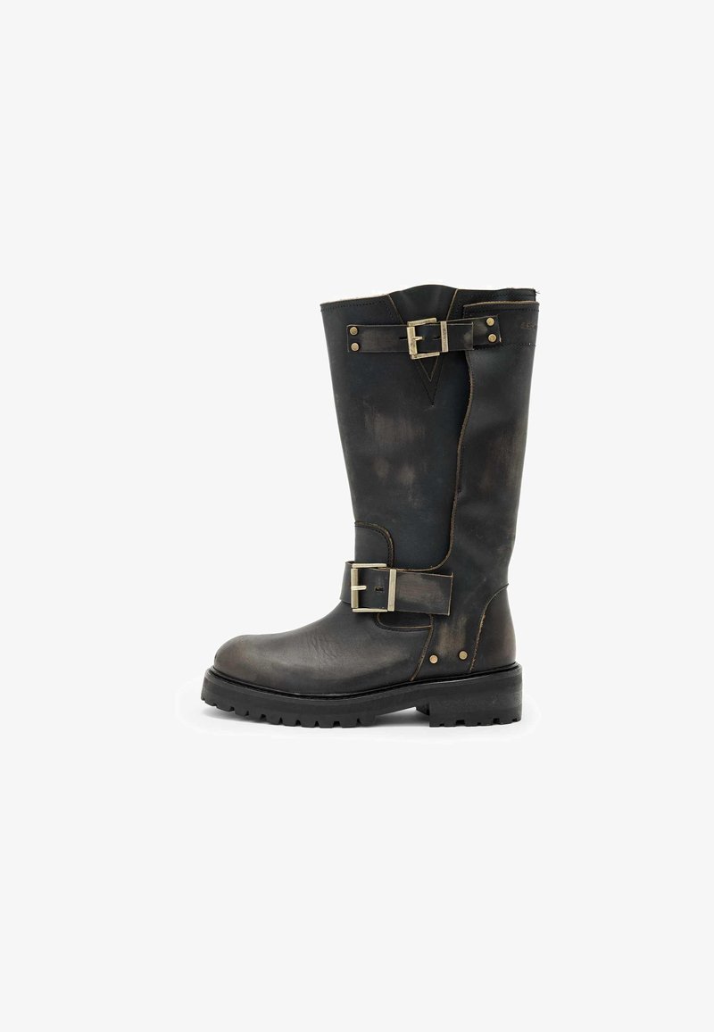 Bota de cuero negro hasta la rodilla con hebillas, superficie texturizada, punta redondeada y suela resistente, diseñada para la durabilidad y el soporte.