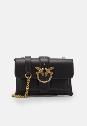 Schwarze Lederhandtasche mit goldener Kettenriemen und dekorativer goldener Ringschnalle, die zwei einander zugewandte Vögel zeigt.