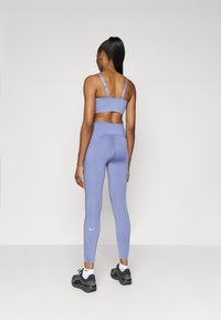 Sostenedor deportivo de color púrpura claro y leggings de tiro alto con detalles de diseño en forma de puntos. La modelo lleva zapatos negros con acentos blancos.