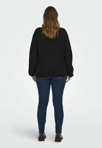 Svart stickad tröja med överdimensionerade långa ärmar, parat med mörkblå slim-fit jeans och svarta plattformsskor, sedd bakifrån.