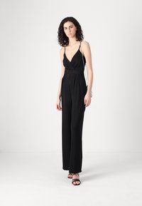 Crni kombinezon s dubokim V-izrezom i tankim naramenicama, suženi struk, široke hlače koje padaju. Model je kombinirao s crnim sandalama i srebrnom torbicom.