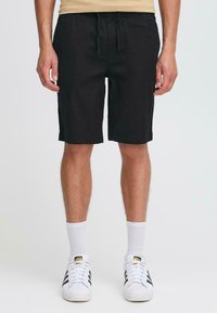 Pantalones cortos de algodón negros con cintura elástica, cordón y bolsillos laterales, combinados con calcetines blancos y zapatillas negras a rayas.