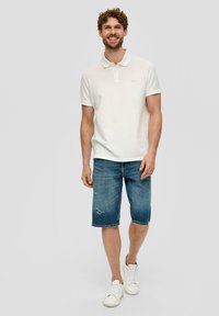 Weißes Poloshirt mit Kragen, Denim-Shorts und weißen Sneakers. Lässiger Schnitt mit ausgewaschener Textur an den Shorts. Neutrale Farben durchgängig.