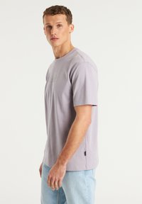 T-shirt a maniche corte di colore viola chiaro con scollatura rotonda e logo ricamato. Realizzato in morbido cotone, presenta una vestibilità comoda e fessure laterali.