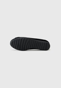 Schwarze Gummisohle mit strukturierten Grip-Mustern und einer abgerundeten Spitze. Das Design ist schlank mit einem minimalistischen Profil.