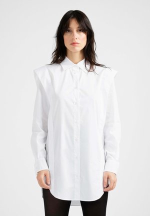 Bela bombažna srajca z oblikovanimi rameni, zapiranjem z gumbi po celotni sprednji strani in dolgimi rokavi. Gladek občutek in rahlo daljši zadnji rob.