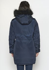 Parka azul marino con capucha desmontable forrada de piel, mangas largas y cintura ceñida. Tejido liso y brillante, de longitud hasta la mitad del muslo.