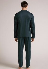 Donkergroene loungewearset met een lange mouwen top en bijpassende broek, gemaakt van een gladde, zachte stof met een comfortabele pasvorm.