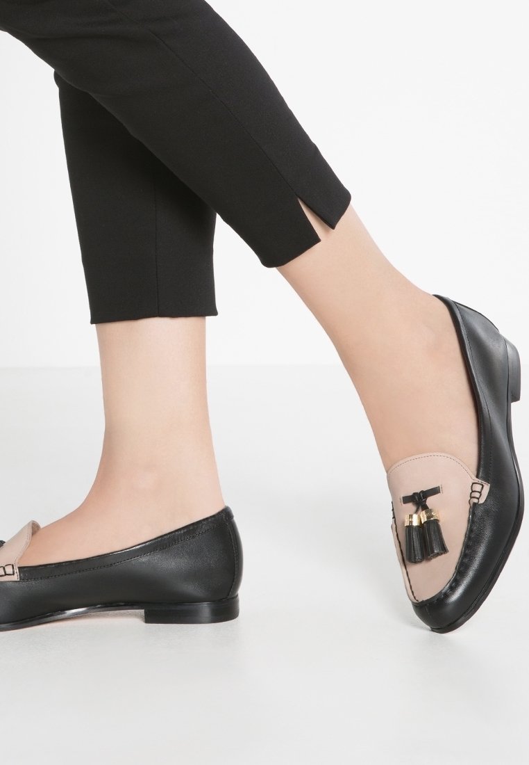 Mocassins noirs et beiges avec une finition en cuir, comprenant un panneau transparent et des ornements à pampilles à l'avant. Conception à bout rond.