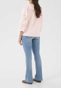 Rosa blus med puffärmar i spets och utskurna mönster. Parat med ljusblå utsvängda jeans och bruna platta skor.