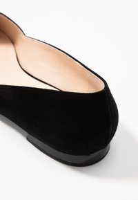 Bailarina negra de ante con puntera redonda, forro interior suave y un bajo tacón negro. El diseño es elegante y minimalista.
