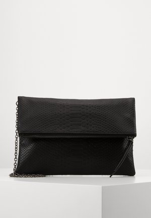 Zwarte gestructureerde clutch met een gevouwen flap en ritssluiting, met een dun metalen kettingriempje op een wit platform.