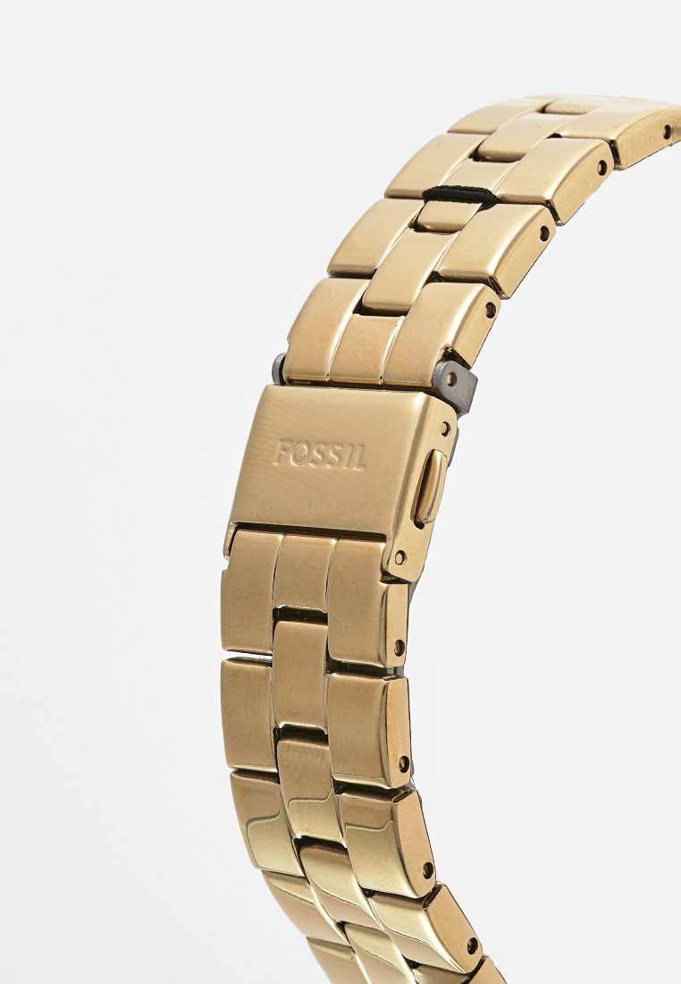 Goldfarbener Metallarmbanduhr mit einem Gliederarmband-Design, das eine polierte Oberfläche aufweist und einen Verschluss hat, der mit "FOSSIL" graviert ist.