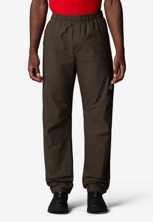 Braune leichte Hose mit elastischem Bund, geraden Beinen und Logodetail am linken Oberschenkel. Getragen mit einem roten Oberteil und schwarzen Schuhen.