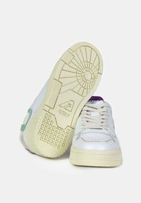 Sneakers in pelle bianca con dettagli verde chiaro, suola in gomma testurizzata, punta rotonda e lacci beige, che mostrano un design atletico classico.