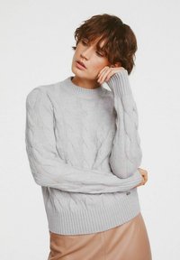 Jasnoszara sweter w splot warkoczowy z okrągłym dekoltem, żebrowanymi mankietami i dołem. Miękka struktura, z wyraźnymi skręconymi wzorami na całej powierzchni.