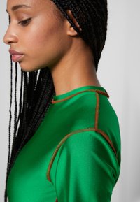 Top de cetim verde com um design justo, apresentando costuras laranja contrastantes ao longo da gola e das costuras dos ombros.