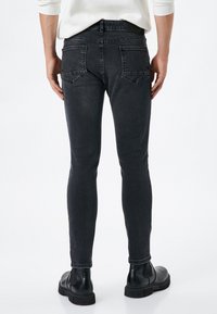 Jeans de denim negro de corte ajustado con una textura desgastada, que presentan dos bolsillos traseros y detalles de costura, combinados con botas negras de tobillo.