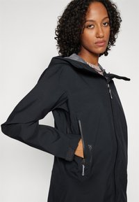 Black waterproof jacket with a hood, side zip pockets, and textured fabric. Features a sleek design and fitted silhouette with gray accents.