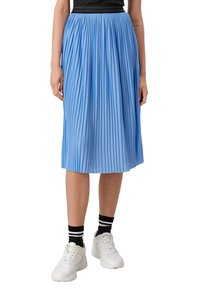 Persona che indossa una gonna plissettata blu chiaro di lunghezza media, calze a righe bianche e nere, sneakers bianche e una maglietta nera.