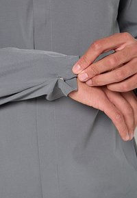 Graues Langarmshirt mit glatter Textur, Knopfverschluss an der Manschette und entspannter Passform. Nahtdetails sind im Stoff sichtbar.