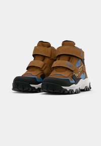 Stivali da trekking marroni e blu con punte nere, suole bianche, battistrada spesso e due fibbie in velcro su ciascun scarponcino.