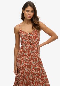 Rdzawoczerwona maxi sukienka w wzór paisley. Ramiączka typu spaghetti, detale z guzikami oraz krój A-linowy z marszczoną talią.