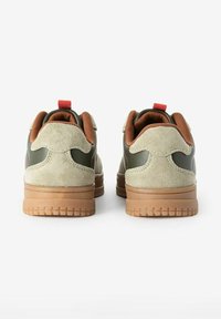 Baskets vertes et beiges avec une tige en daim et cuir, dotées d'un col rembourré marron, d'un onglet au talon rouge et d'une semelle en caoutchouc texturée.
