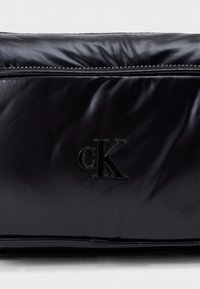 Μαύρη τσάντα από ελαστικό νάιλον με υφή, με κρυφό φερμουάρ και ανάγλυφο λογότυπο. Συμπαγές ορθογώνιο σχήμα.