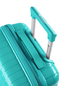 Valigia rigida turchese con texture a righe, dotata di manico metallici retrattile e chiusura a zip. Design robusto, con accenti minimi.