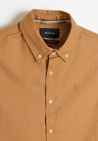Brązowa koszula zapinana na guziki, wykonana z mieszanki bawełny, z klasycznym kołnierzykiem, subtelną fakturą i wyszywanym logo po lewej stronie.